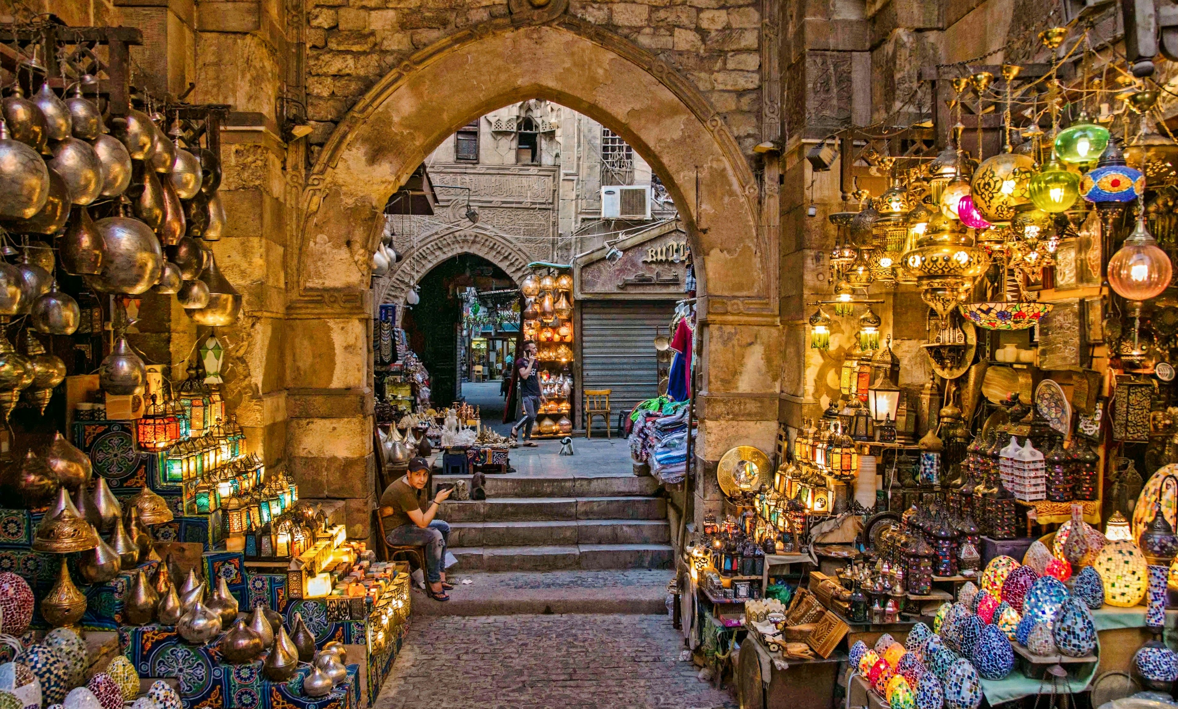 Ruelle d'un souk bordée d'échoppes remplies de lanternes artisanales sous des arches en pierre