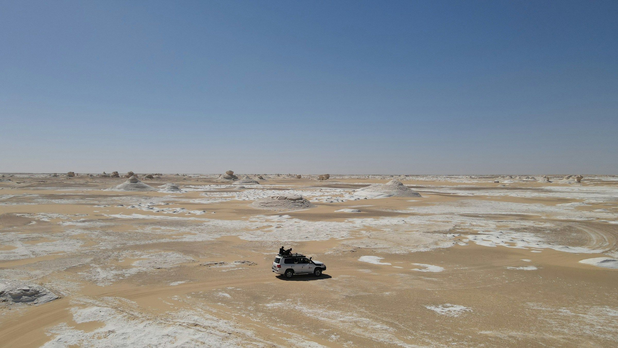 Voyage en Egypte - Vue aérienne d'un 4x4 roulant sur le désert blanc